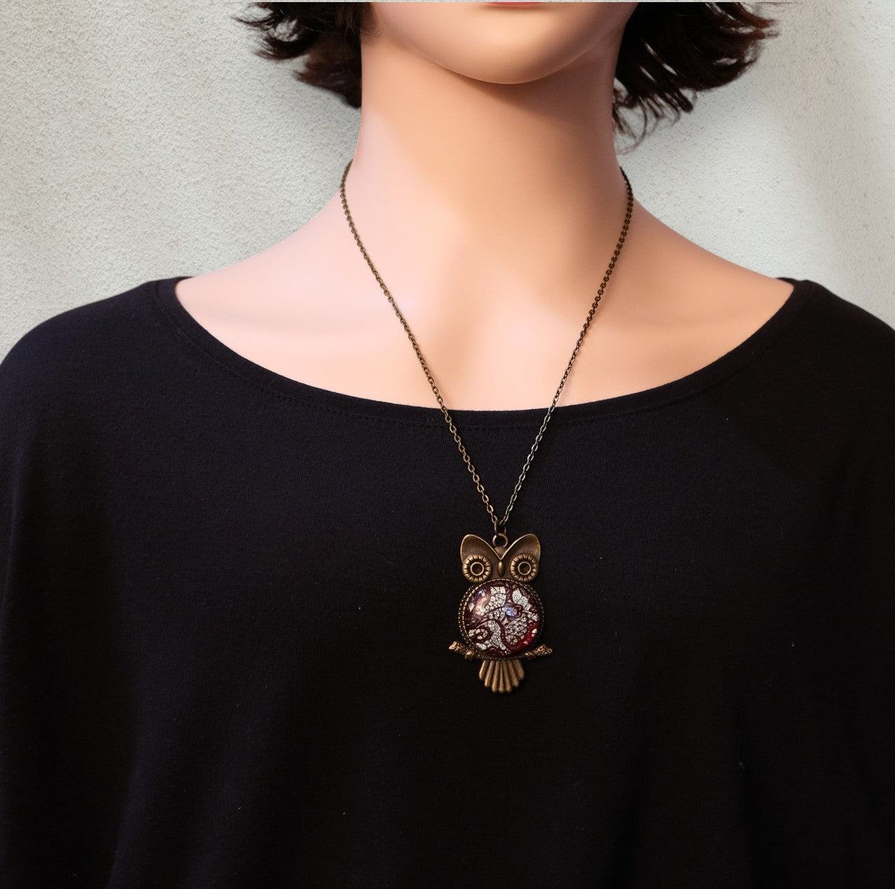Person wearing a black shirt with an owl pendant necklace.