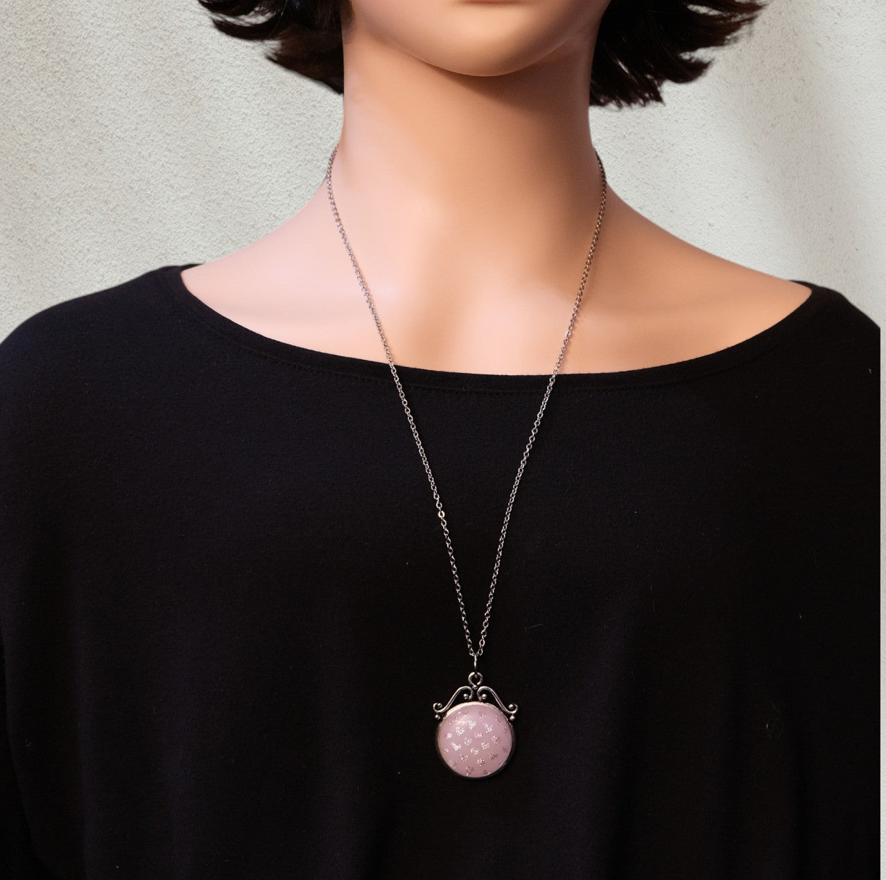 Mannequin wearing a black top with a pink pendant necklace