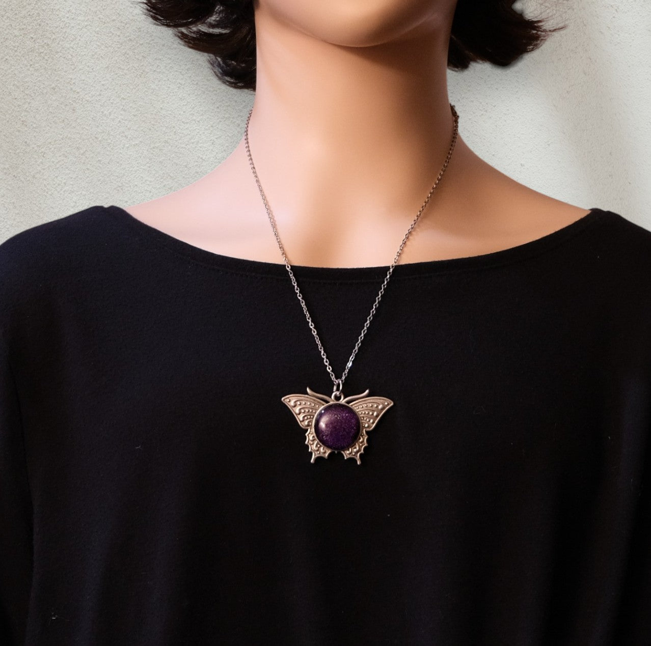 Person wearing a necklace with a purple pendant on a plain background