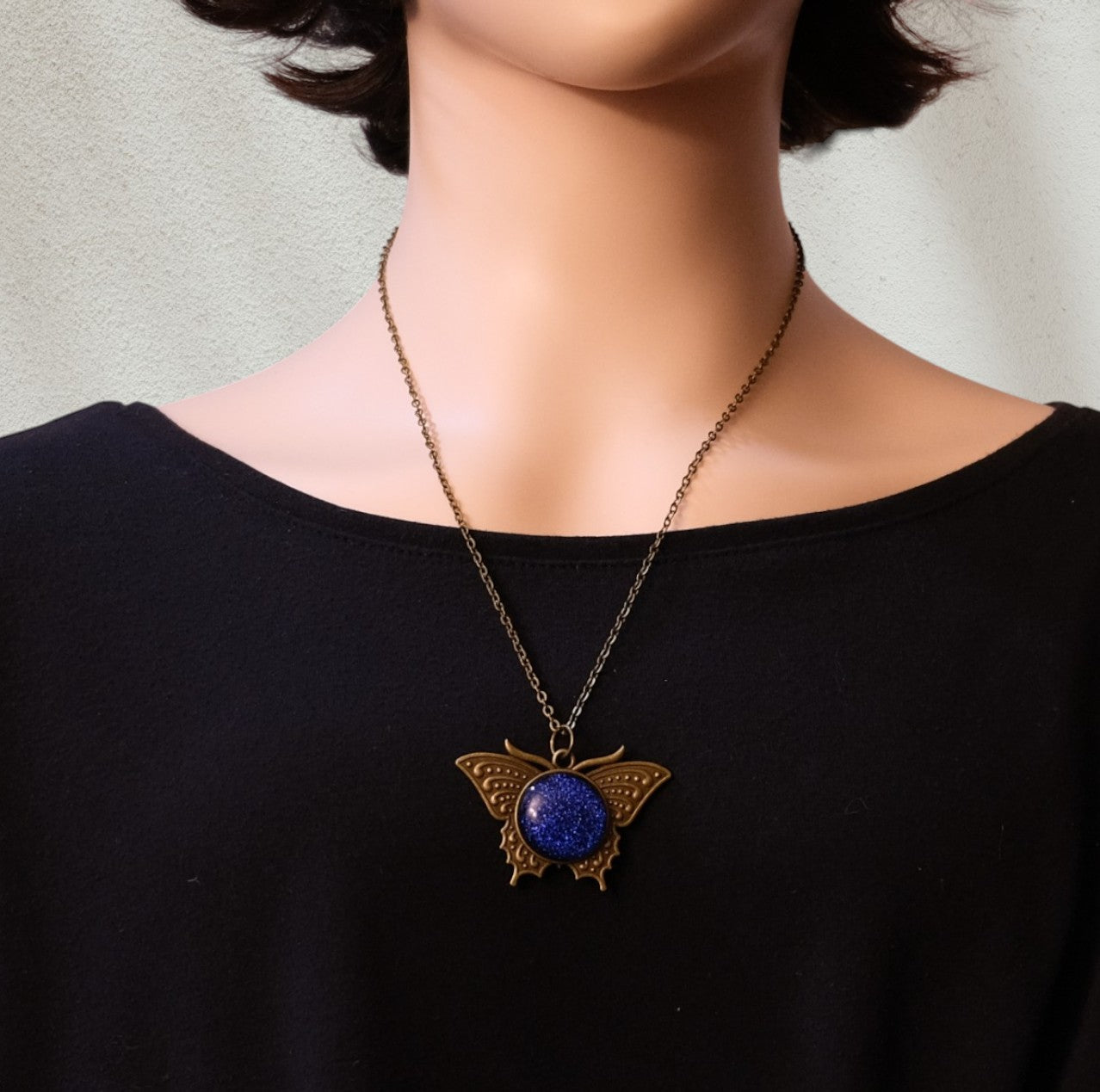 Butterfly necklace with a blue pendant on a person wearing a black top.