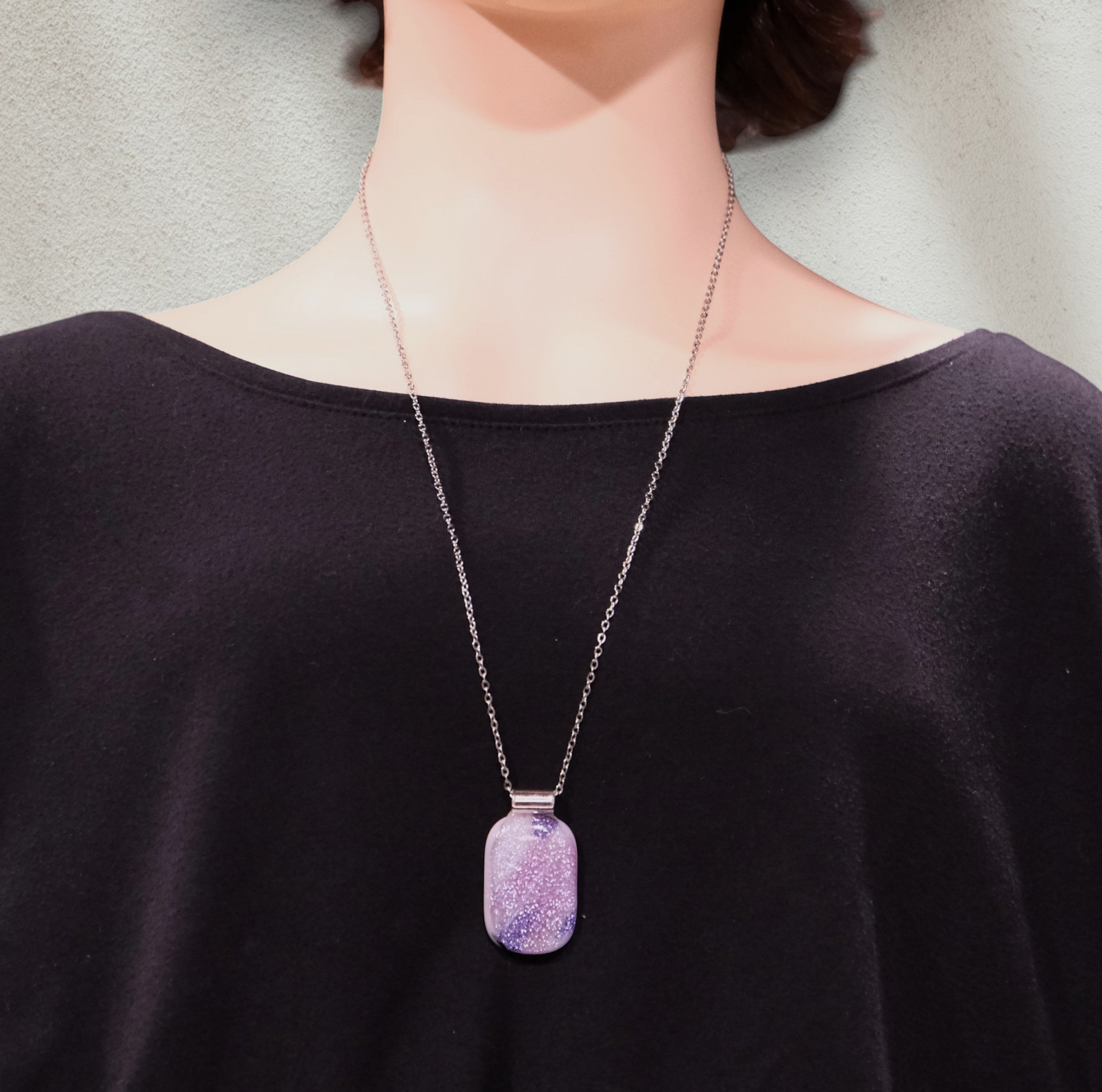 Person wearing a necklace with a purple pendant against a neutral background