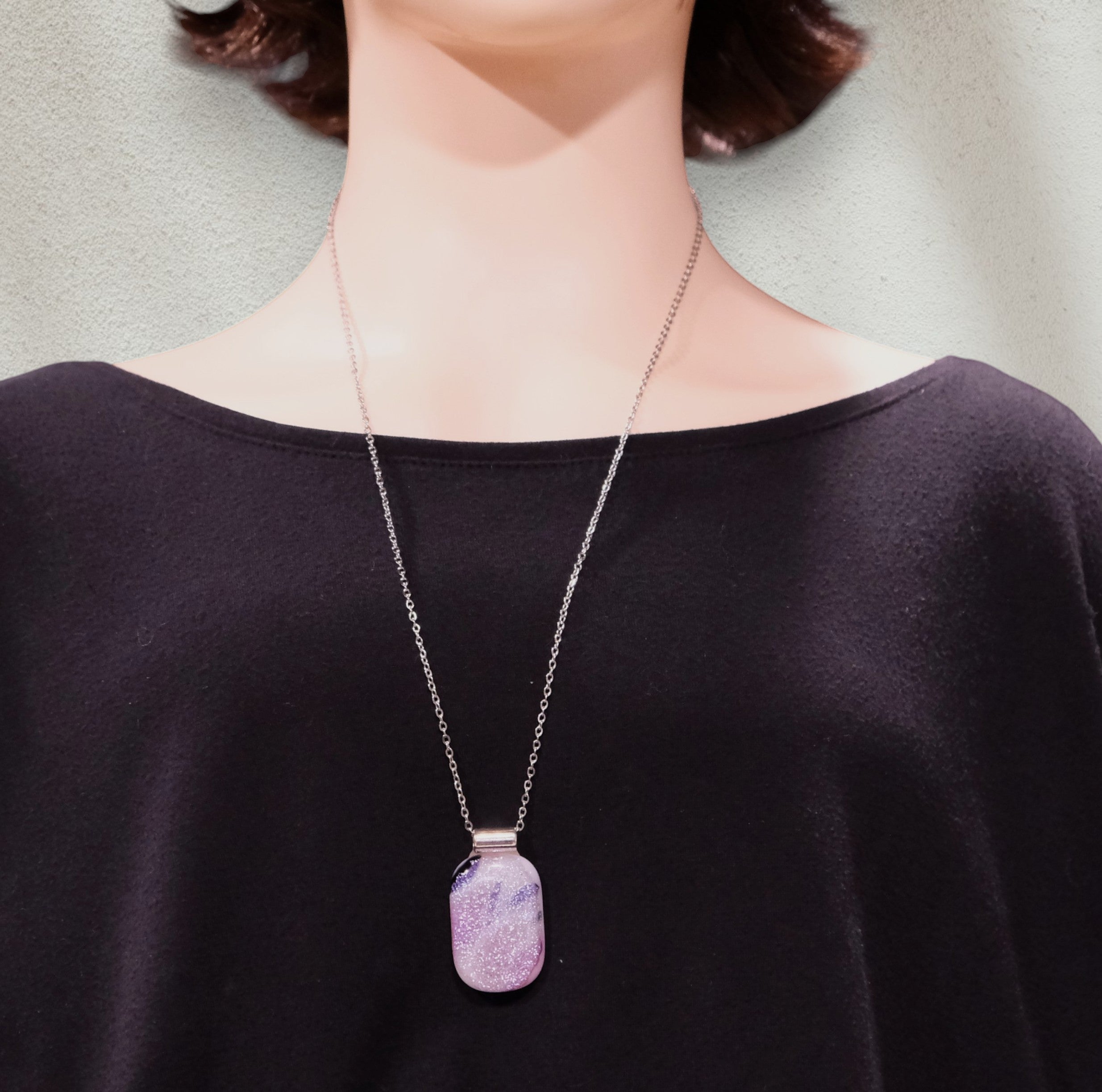 Person wearing a necklace with a purple pendant against a neutral background
