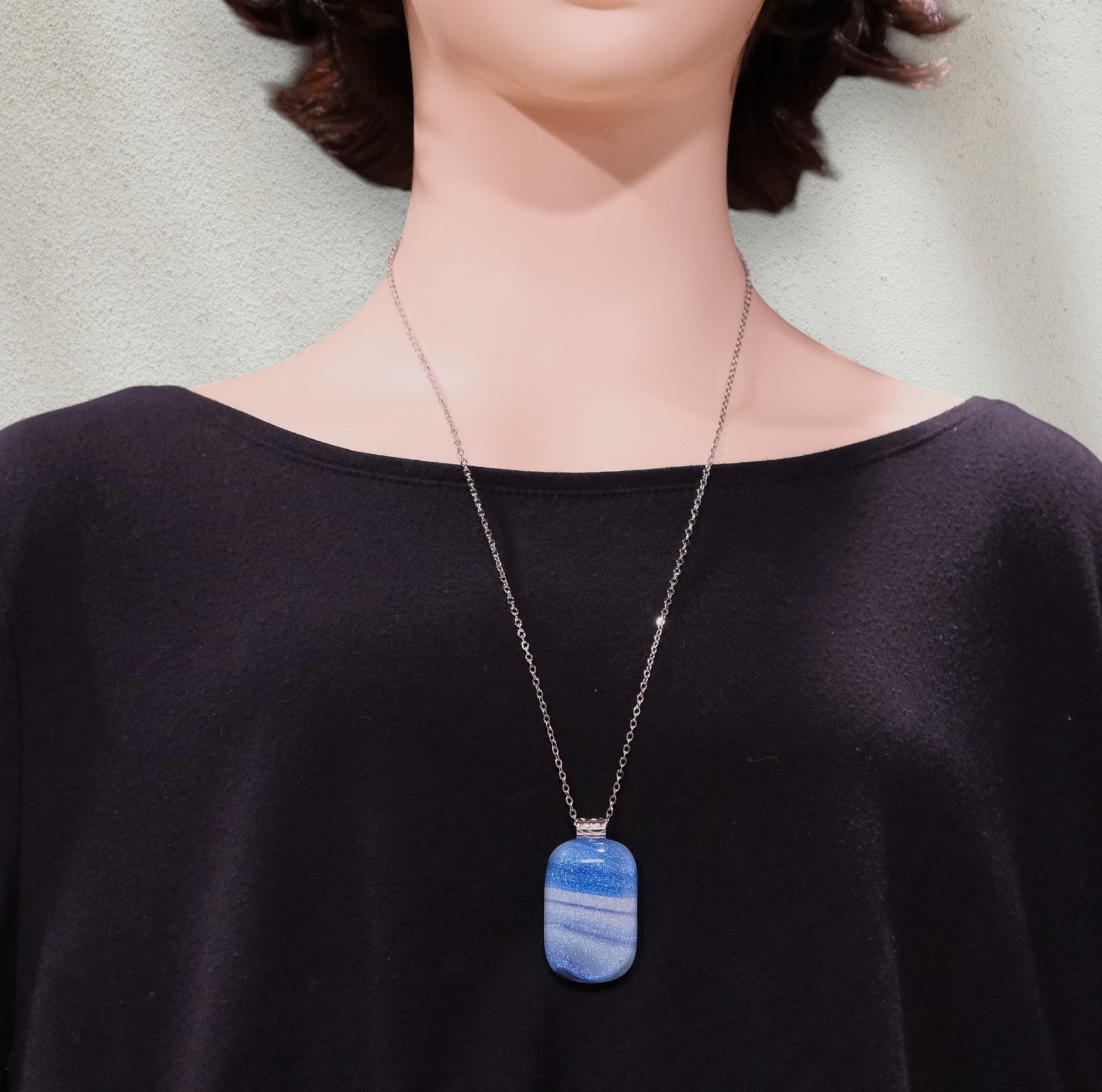 Person wearing a necklace with a blue pendant against a neutral background