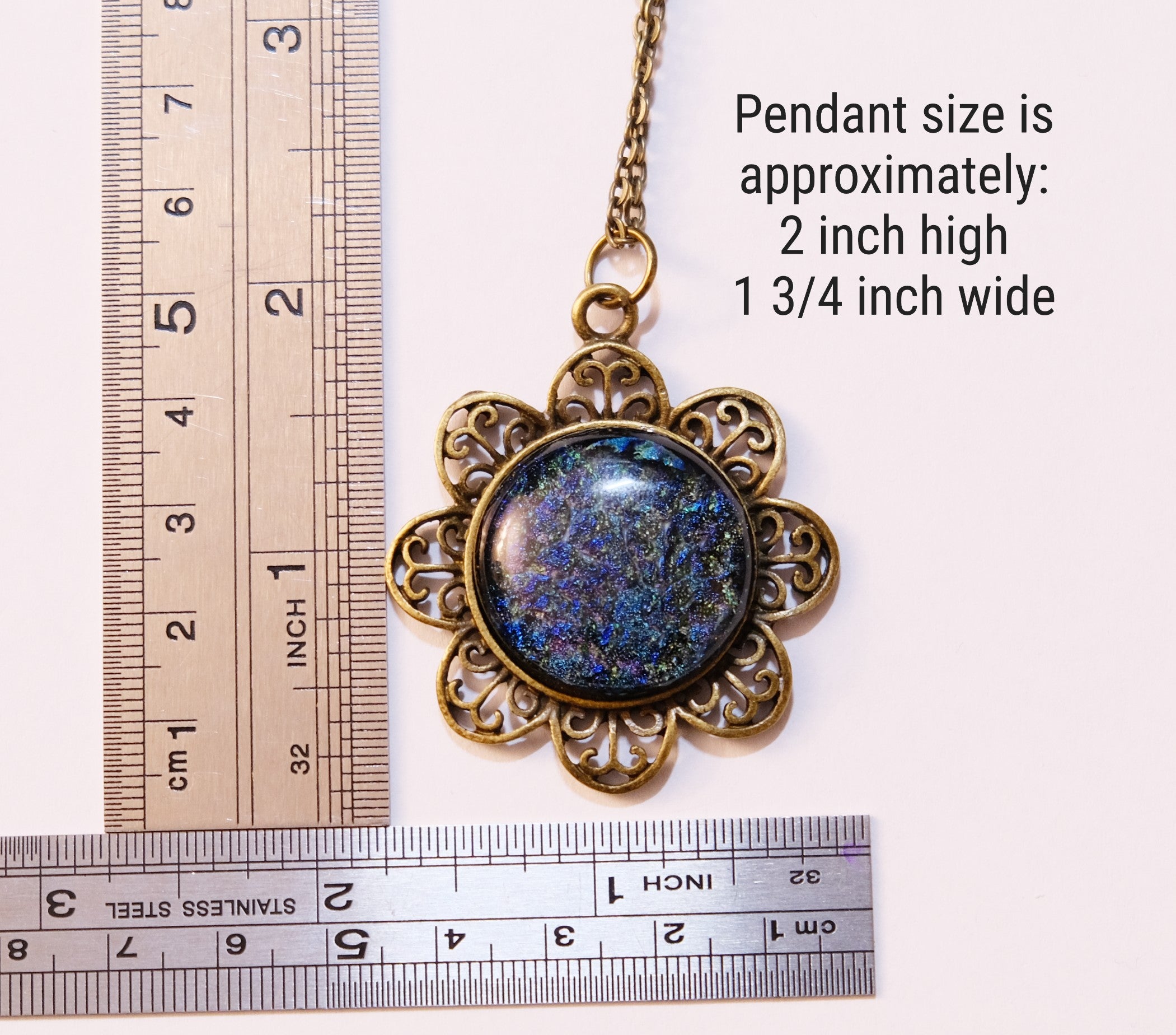 Decorative pendant with a blue stone and gold frame, shown with two rulers for size reference.