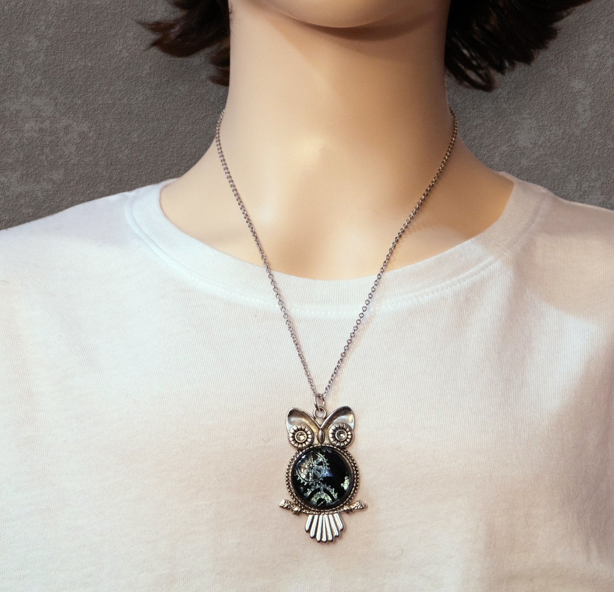 Necklace with an owl pendant worn by a person on a plain background