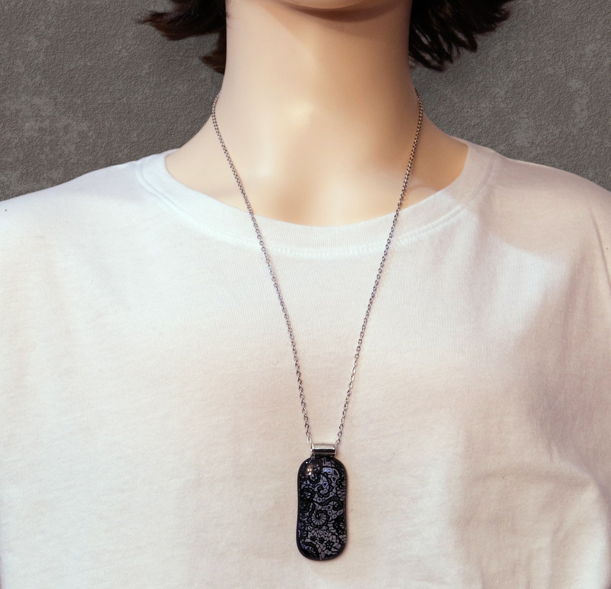 Person wearing a necklace with a black pendant on a plain background