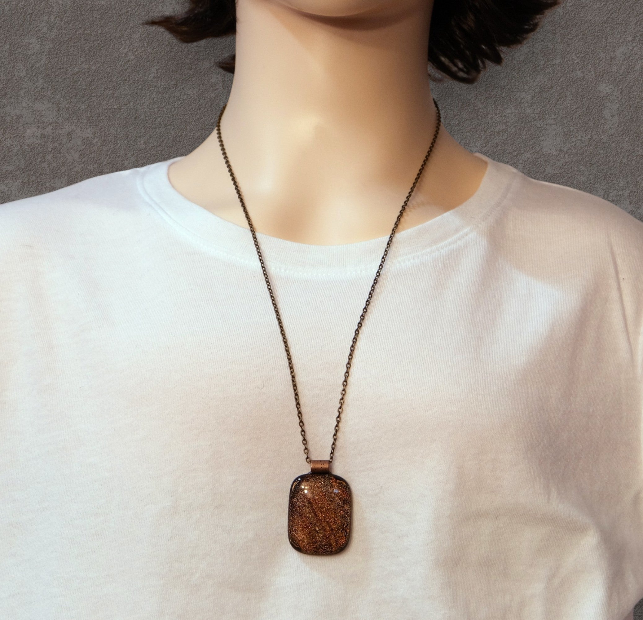Person wearing a necklace with a brown pendant on a plain background