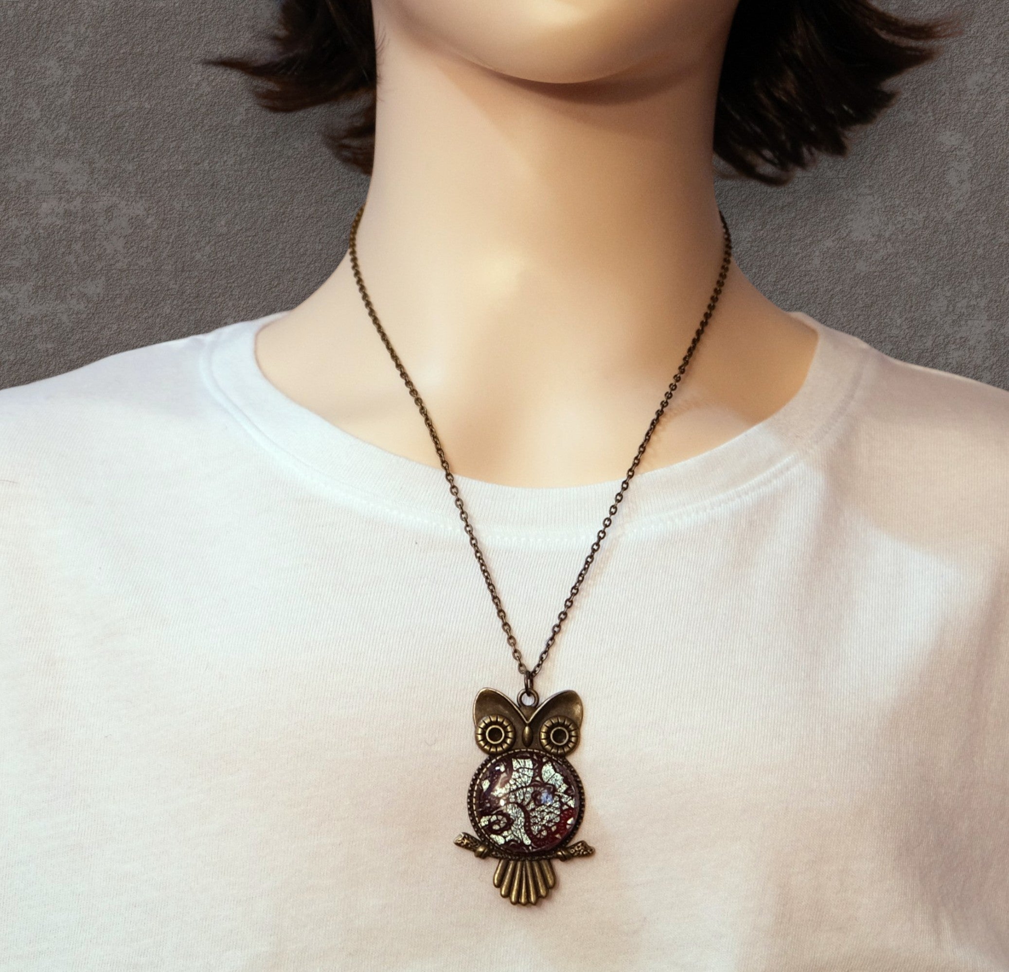 Necklace with an owl pendant worn by a person on a plain background