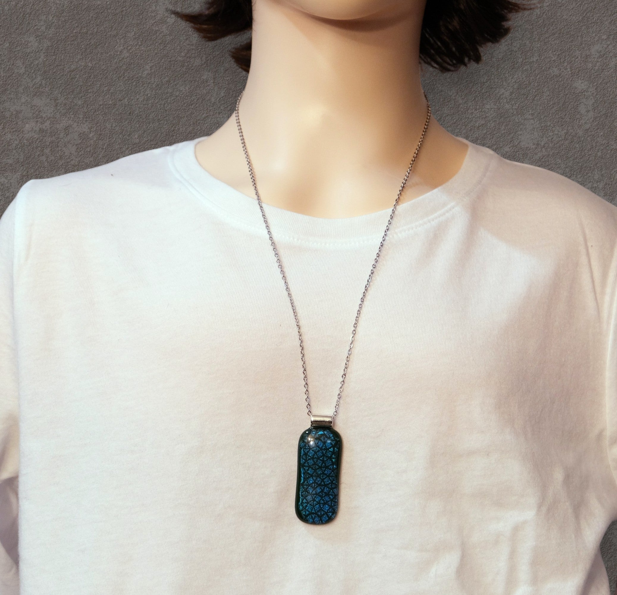 Person wearing a necklace with a blue pendant on a plain background