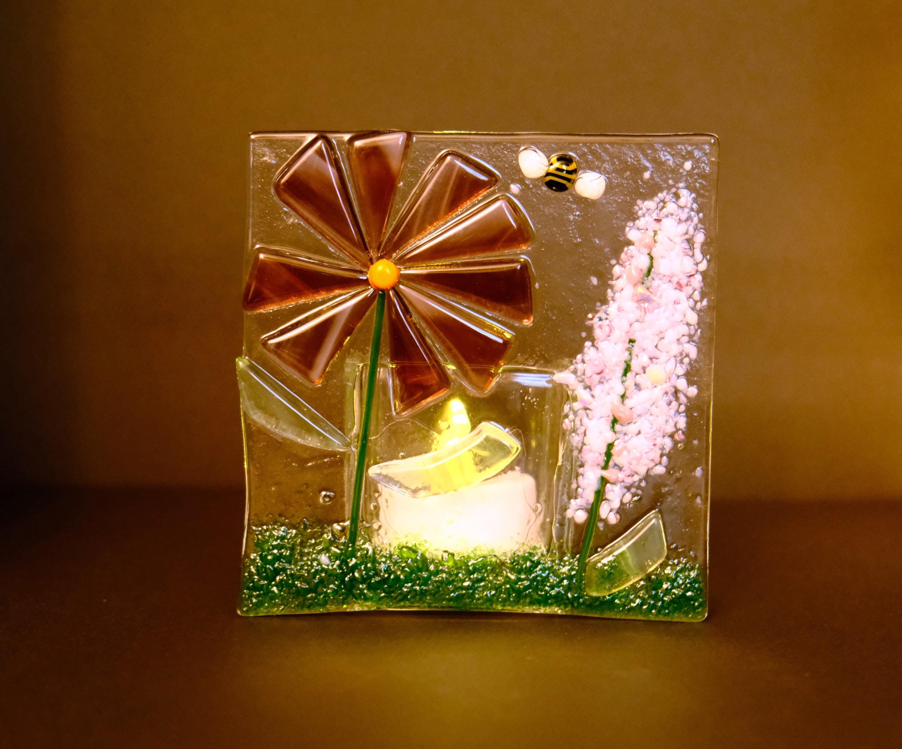 Decorative glass panel with a flower, candle, and bee on a dark background